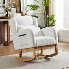 a white rocking chair sitting on top of a hard wood floor next to a potted plant