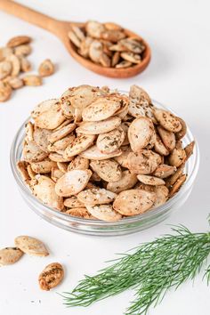 a glass bowl filled with cashews next to a wooden spoon and sprig of rosemary