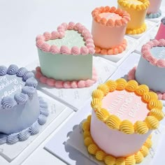 there are many cakes on the table with different frosting shapes and colors, including pink, blue, yellow, and white