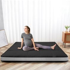 a pregnant woman sitting on a mattress in the middle of a room