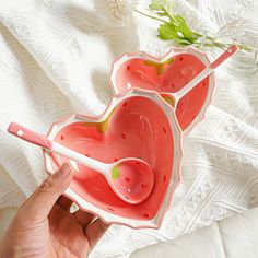 two pink heart shaped bowls with spoons in them on a white surface next to a flower