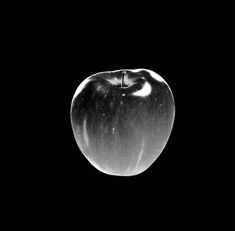 black and white photograph of an apple in the dark with water droplets on it's surface