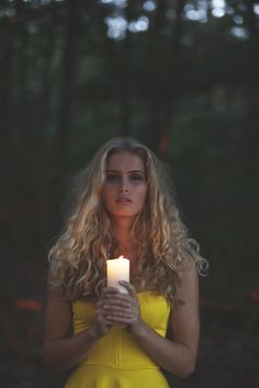 a woman in a yellow dress holding a candle