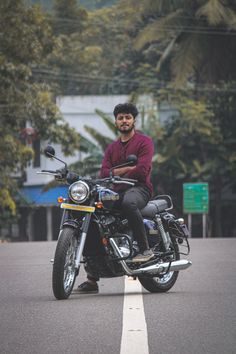 a man is sitting on his motorcycle in the middle of the road with trees behind him