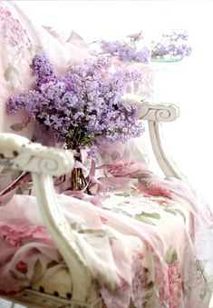 purple flowers are sitting in a vase on a white chair with pink fabric draped over it