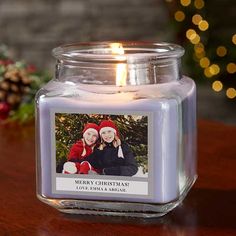 a candle that is sitting on a table next to a christmas tree with lights in the background