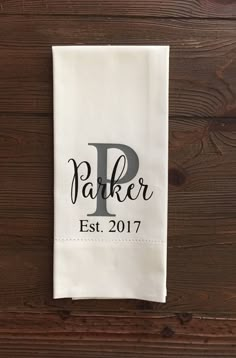 a personalized tea towel hanging on a wooden wall with the word parker est 2017 printed on it