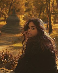 a woman sitting on a park bench talking on a cell phone with trees in the background