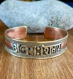 "This beautiful Om Namah Shivaya cuff bracelet is made in Nepal. Size: 18cm - As It's open-ended, would fit most hands Width - 15mm approx Weight - 23gms approx Material: white metal, brass, copper To fit the bracelet open it up so the gap is wide enough to pass over the narrowest part of your wrist and then squeeze it back into shape until it is a nice comfortable fit. Om Namah Shivaya (Devanagari: ॐ नमः शिवाय;[1] IAST: Om Namaḥ Śivāya) is one of the most popular Hindu mantras and the most impo Traditional Bangle Wristband As Gift, Symbolic Handmade Bracelets For Festivals, Handmade Symbolic Beaded Bangle Bracelet, Adjustable Spiritual Bangle Bracelet, Symbolic Bangle Bracelets For Festivals, Unique Cuff Bracelet For Festivals As A Gift, Handmade Symbolic Beaded Bangle Bracelets, Symbolic Cuff Bangle Bracelet As Gift, Adjustable Cuff Bangle In Traditional Style