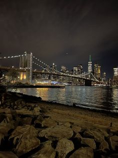 the city skyline is lit up at night by the water and rocks on the shore