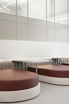 two round tables with brown leather seats in front of them and a white wall behind them