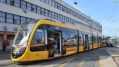 a yellow train traveling past a tall building