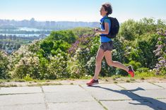 a woman with a backpack is running on a path in the park near flowers and trees