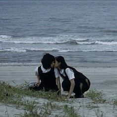 two people are kissing on the beach by the water's edge with grass in front of them