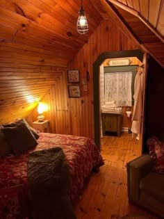 an attic bedroom with wood paneled walls and wooden flooring is lit by a lamp