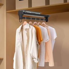 three shirts hanging on a rail in a closet next to a coat rack with clothes