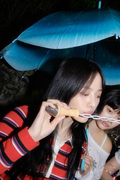 two young women standing under umbrellas blowing bubbles on their heads, one woman is holding an umbrella up to her mouth