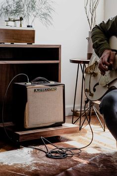 a man sitting on the floor playing an electric guitar next to a small table with a plant in it