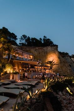 an outdoor area with lights and plants at night, next to a cliff side restaurant