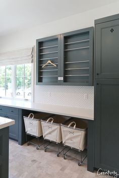 a kitchen with gray cabinets and white counter tops, two laundry baskets on the island