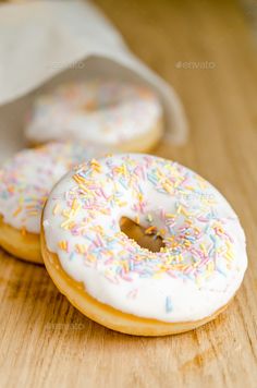 two donuts with white frosting and sprinkles on a wooden table