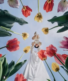 a woman standing in front of flowers with her hands up to the sky above her head