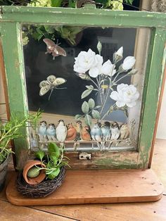 an old frame with flowers and birds in it on a table next to a potted plant