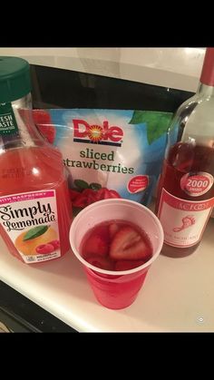 a bottle of juice and some strawberries in a cup on a counter next to other drinks