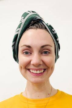 a smiling woman wearing a green and white head scarf on her head with a yellow shirt