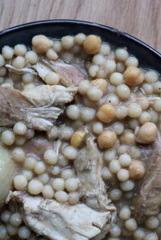 a bowl filled with meat and beans on top of a wooden table