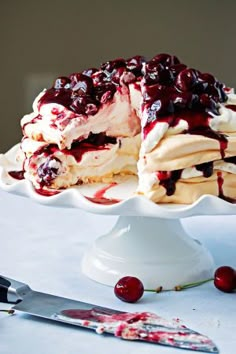 a cake with white frosting and cranberry toppings on a plate next to a knife