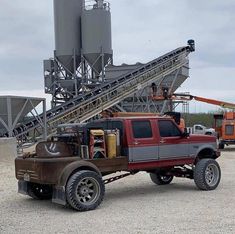 a red truck parked in front of a cement silo with a crane on it's back