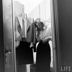 a black and white photo of a woman looking at clothes