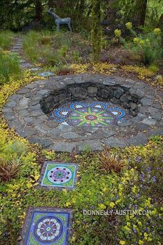 a garden with flowers and plants surrounding it, including an outdoor fire pit in the middle