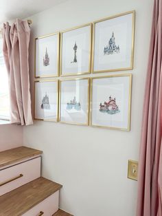 four framed pictures hang on the wall next to pink curtains and wooden steps in front of a window