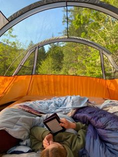 a person laying in a tent reading a book and looking at something on the ground