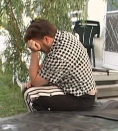 a man sitting on the ground in front of a house with his hands to his face