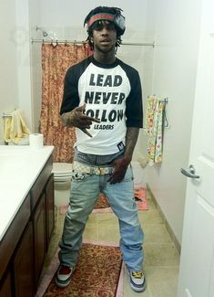 a man standing in front of a bathroom sink wearing jeans and a t - shirt that says lead never follow