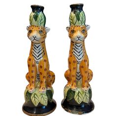 pair of ceramic tiger figurines sitting side by side on black bases with green leaves