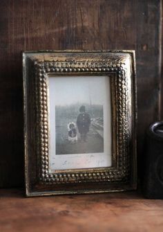 an old photo frame sitting on top of a wooden table next to a cup and candle