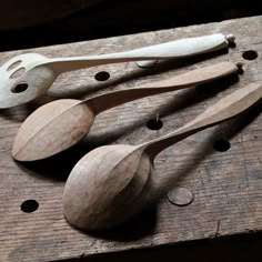 three wooden spoons and two white plastic spoons on top of a piece of wood