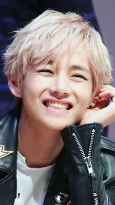 a young man with blonde hair wearing a black leather jacket and smiling at the camera