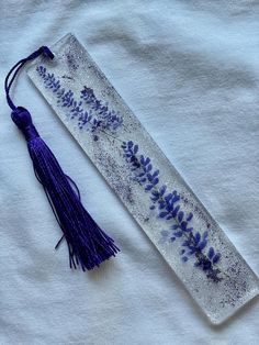 a purple tasseled bookmark with flowers and leaves on it sitting on top of a white t - shirt