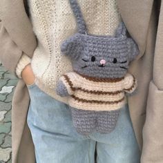 a crocheted cat holding a sweater on it's back while standing next to a woman