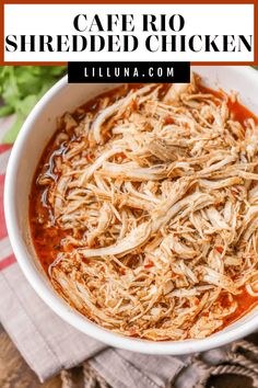 a white bowl filled with shredded chicken on top of a wooden table next to a napkin