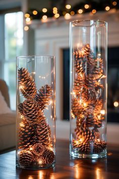 two glass vases filled with pine cones on top of a table next to a fireplace