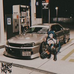 a woman sitting on the ground next to a car in front of a gas station