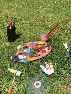 paintbrushes, palettes and other art supplies sit on the grass