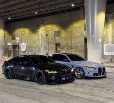 two black and silver cars are parked in an empty parking garage with concrete flooring