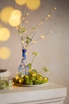 a blue vase filled with flowers sitting on top of a white table covered in lights